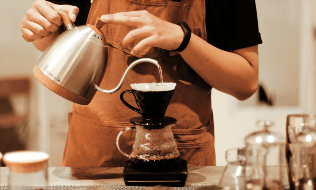  Using a gooseneck kettle, the barista pours hot water in a controlled, circular motion over freshly ground african coffee in a dripper